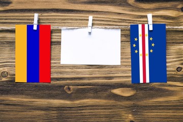 Hanging flags of Armenia and Cape Verde attached to rope with clothes pins with copy space on white note paper on wooden background.Diplomatic relations between countries.