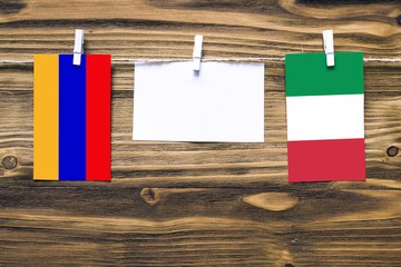 Hanging flags of Armenia and Italy attached to rope with clothes pins with copy space on white note paper on wooden background.Diplomatic relations between countries.