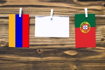 Hanging flags of Armenia and Portugal attached to rope with clothes pins with copy space on white note paper on wooden background.Diplomatic relations between countries.