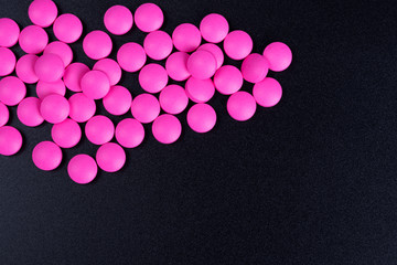 Pink pills are scattered on a black background.