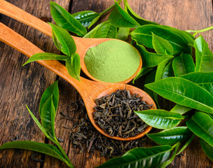 heap of dried green tea leaf and powder on wooden background