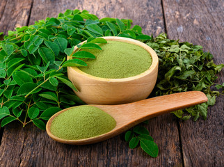 Moringa powder in wooden bowl with  fresh Moringa and dried leaves  on wooden background