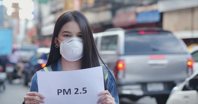 Young woman in protective mask holding pollution problem sign at city.