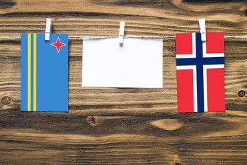 Hanging flags of Aruba and Norway attached to rope with clothes pins with copy space on white note paper on wooden background.Diplomatic relations between countries.