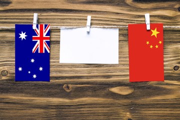 Hanging flags of Australia and China attached to rope with clothes pins with copy space on white note paper on wooden background.Diplomatic relations between countries.