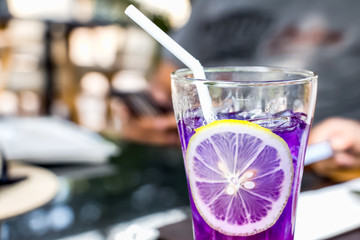 Purple ice cold modern gourmet craft cocktail of tonic soda garnished and lemon slice on bar with blurry restaurant bar background.