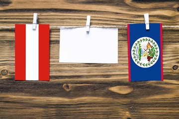 Hanging flags of Austria and Belize attached to rope with clothes pins with copy space on white note paper on wooden background.Diplomatic relations between countries.
