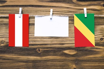 Hanging flags of Austria and Republic Of The Congo attached to rope with clothes pins with copy space on white note paper on wooden background.Diplomatic relations between countries.