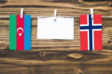 Hanging flags of Azerbaijan and Norway attached to rope with clothes pins with copy space on white note paper on wooden background.Diplomatic relations between countries.