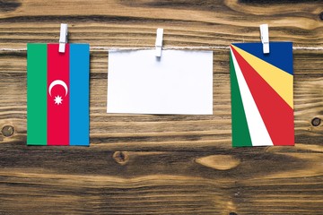Hanging flags of Azerbaijan and Seychelles attached to rope with clothes pins with copy space on white note paper on wooden background.Diplomatic relations between countries.