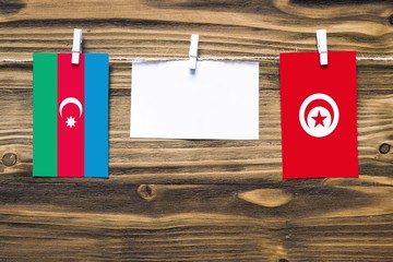 Hanging flags of Azerbaijan and Tunisia attached to rope with clothes pins with copy space on white note paper on wooden background.Diplomatic relations between countries.