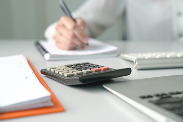 Office table view with Accountant or Woman Executive out of focus and focus is on calculator