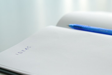 Open blank notepad with pen and the word Ideas written on it.