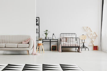 Beige trendy sofa in scandinavian design kid's bedroom with industrial furniture and patterned black and white rug on the floor, copy space on empty wall