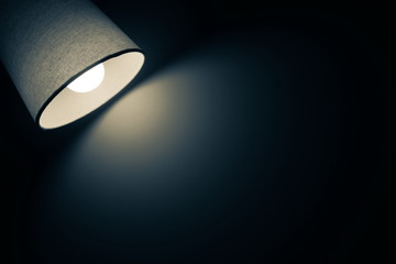 Dark and vintage mood of a desk lamp shining warm light in the dark room in black and blue tone with copy space for add text Living home and office interior concept