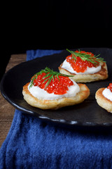 Pancakes with red caviar and cream cheese topped with dill on black plate
