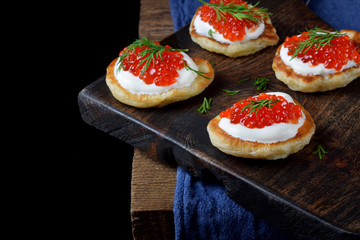 Pancakes with red caviar and cream cheese topped with dill on the wooden board