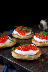 Pancakes with red caviar and cream cheese topped with dill on the wooden board