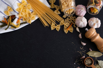 Flat lay Ingredients for cooking Italian pasta on black stone slate - fettuccine, spaghetti, tomatoes, basil, oil and garlic. Italian food. Top view with space for text.