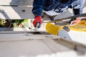 Construction worker plastering a wall with trowel cement mortar applying adhesive cement on the Autoclaved aerated concrete AAC brick high angle close up on hand holding the tool outdoor