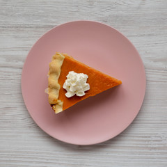 Top view, homemade Thanksgiving pumpkin pie on a pink plate on a white wooden background. Overhead, from above, flat lay. Close-up.