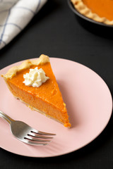 Homemade Thanksgiving pumpkin pie on a pink plate on a black background, side view. Closeup.
