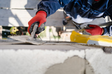 Construction worker plastering a wall with trowel cement mortar applying adhesive cement on the Autoclaved aerated concrete AAC brick high angle close up on hand holding the tool outdoor