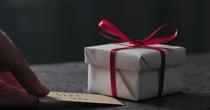 Slow motion man hand put greeting paper card next to white gift box on terrazzo countertop