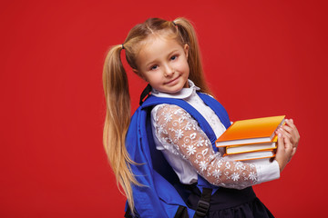 Portrait of little schoolgirl with notebooks, wearing white blouse, on a red background