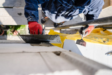 Construction worker plastering a wall with trowel cement mortar applying adhesive cement on the Autoclaved aerated concrete AAC brick high angle close up on hand holding the tool outdoor