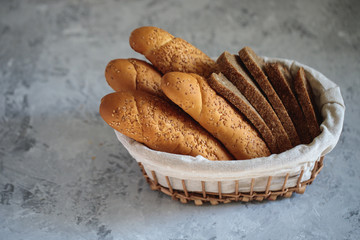 Fresh bread baguette with sesame seeds and slices of rye bread are in the breadbox on the table. Bakery. Flat lay. Close-up, minimalism. - obrazy, fototapety, plakaty