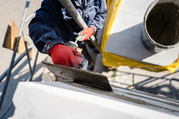 Construction worker plastering a wall with trowel cement mortar applying adhesive cement on the Autoclaved aerated concrete AAC brick high angle close up on hand holding the tool outdoor