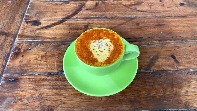 Top view of a turmeric latte with coconut milk and cinnamon powder on top. Vegan health drink served in a green cup. Golden milk drink.
