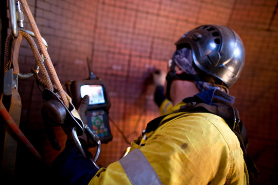 Male rope access UT technician inspector wearing safety harness working at height ascending on twin rope commencing wall thickness defect inspection construction at Pilbara mine site, Perth, Australia