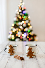 Merry Christmas! Christmas tree-shaped gingerbread cookie near cups of tea. Beautiful blurred christmas tree background with luminous garland.