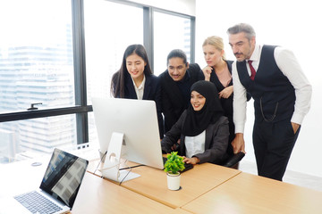 Senior manager and all members in the team helping their Muslim colleague solve the problems on the computer screen in the office