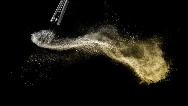 golden powder splash and brush for makeup artist or graphic design in black background
