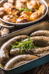 Roasted sausages in pan with rosemary and potatoes.. Traditional european food bratwurst jaternice or jitrnice