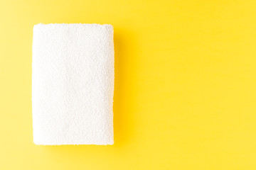 White spa towel on yellow background with copyspace. Top view