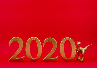 Golden figures 2020 and toy dinosaur over the red background. New year celebration