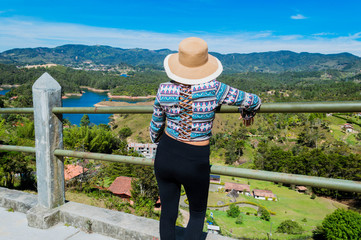 Fototapeta na wymiar Vista trasera de mujer turista con sombrero contemplando la naturaleza en Guatape Colombia desde la piedra del peñol