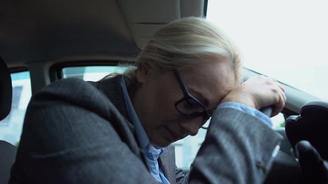 Upset woman leaning on steering wheel and crying, professional burn-out, pms