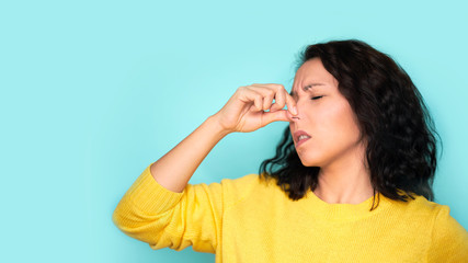 woman smelling something stinky and disgusting, intolerable smell, holding breath with fingers on nose. Bad smells