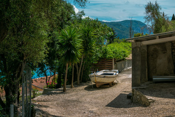 View of old fisher boat, palm and olive trees, green bushes, blue sky and mountains on the horizon