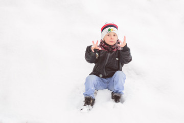 Fototapeta na wymiar The boy fell in the snow and got his hands dirty, they froze and he looks at them in surprise