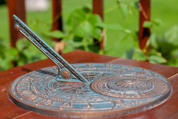 Antique sundial with a beautiful dial and ornament. The bronze oxidized disk is located on a wooden base. Selective shallow focus on the center of the disc.