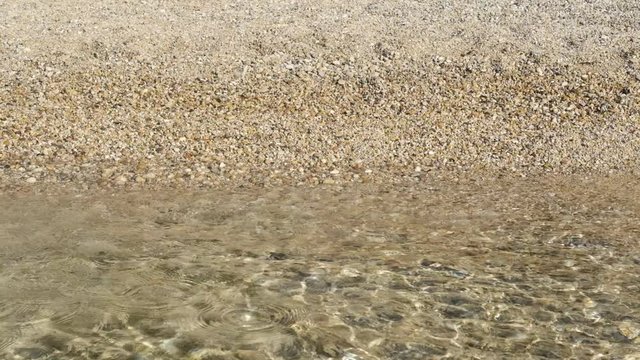 Sea water surface at the pebble beach. Beautiful sun beams in ripple waves.