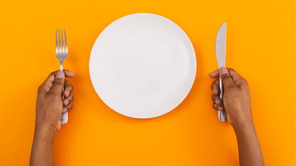 Empty plate and cutlery in woman's hands on orange background