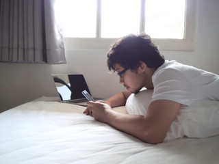 Young Asian man with mobile smart phone lying down on the bed in morning