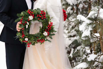 Winter wedding. Bride and groom holding Christmas wreath